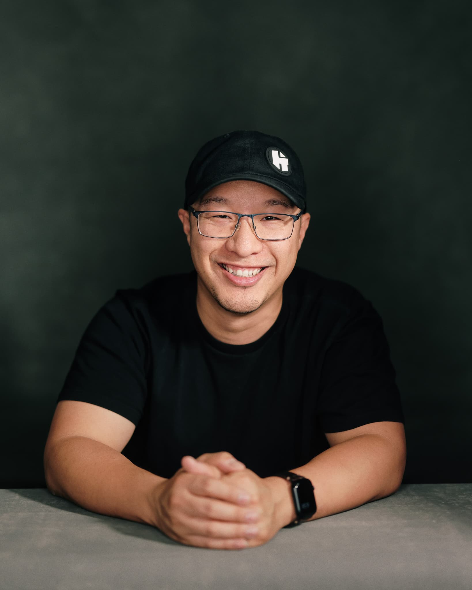 Kevin Thai, founder of Three Circles Studio, smiling with hands clasped, studio portrait against a dark green background.