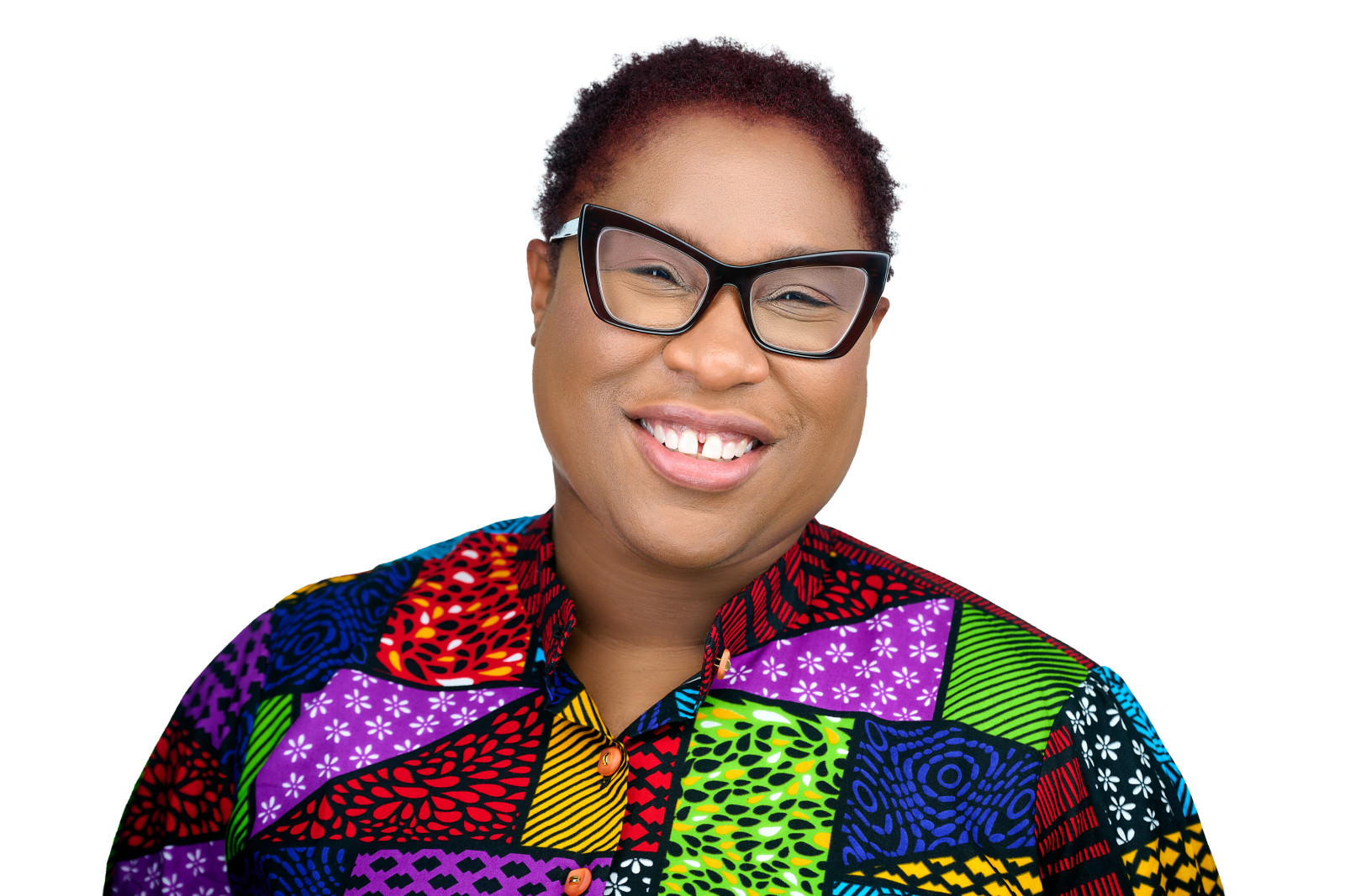 Professional headshot of a smiling woman wearing glasses and a colorful patterned shirt, white studio background
