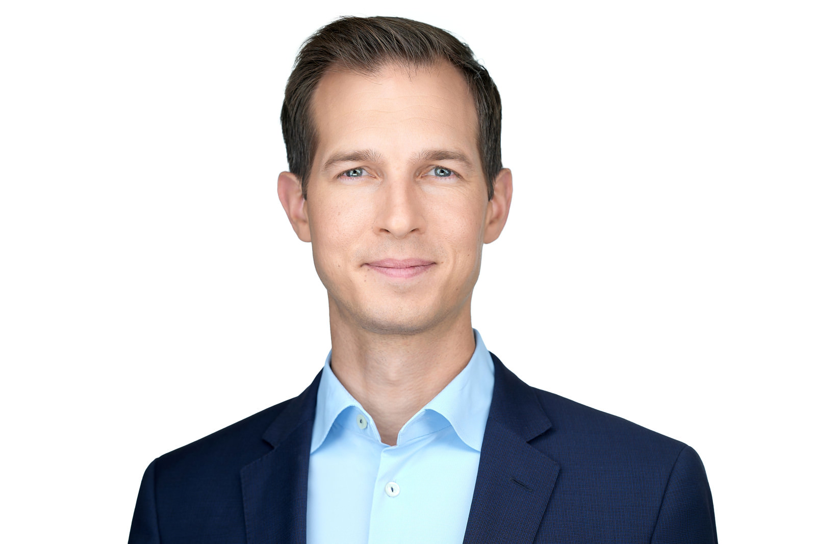 Professional headshot of a smiling man with brown hair wearing a navy blazer, white studio background