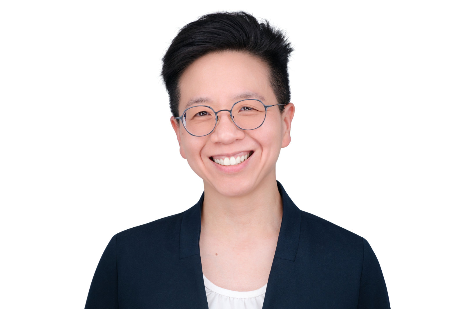 Professional headshot of a smiling person wearing round glasses and a navy blazer, white studio background